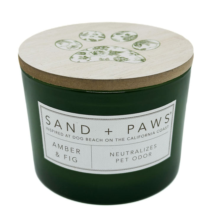 Amber & Fig Scented Candle by SAND + PAWS. Green candle with a wooden lid labeled 'Sand + Paws' on a white background