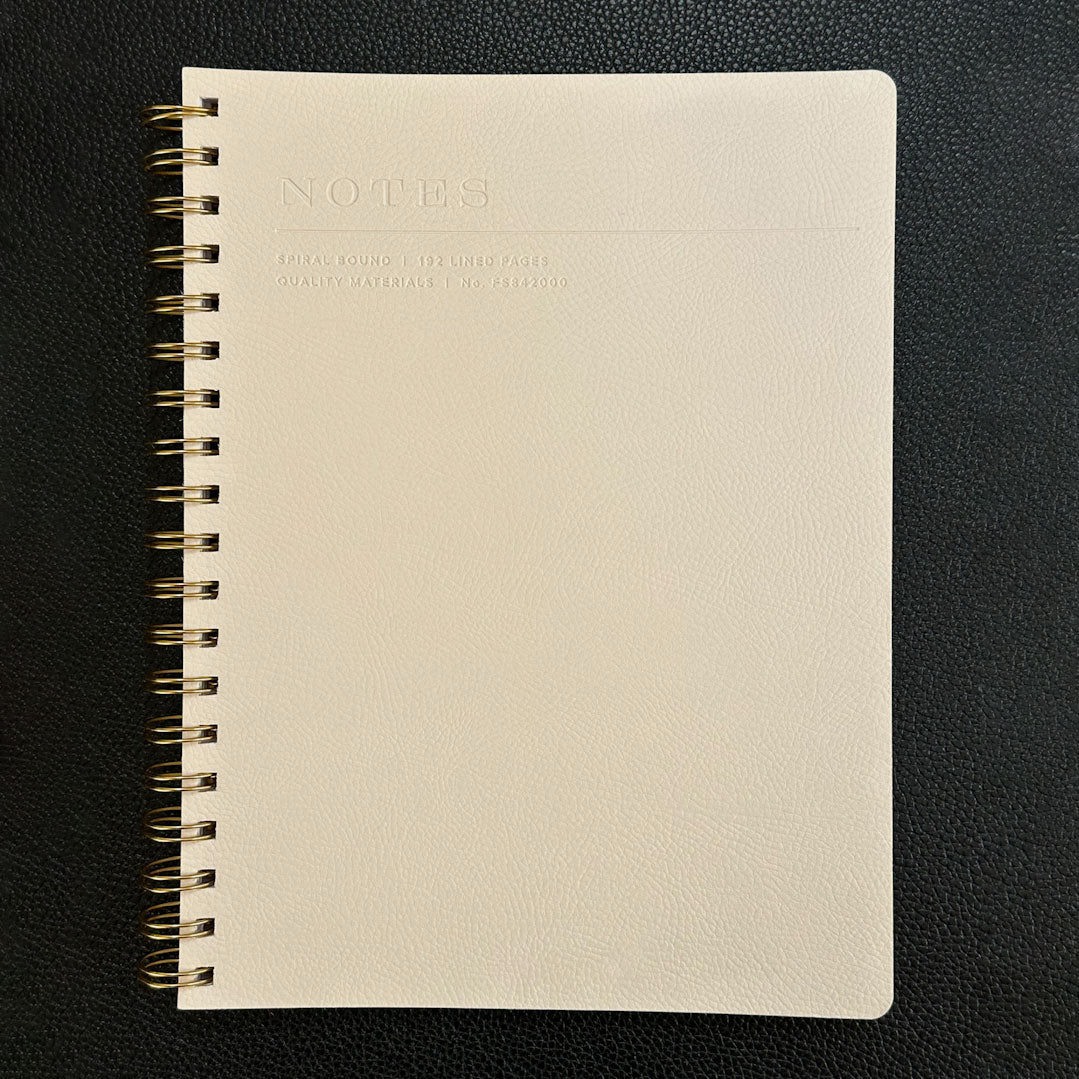 Fringe Studio beige notebook with gold spiral binding on a black background