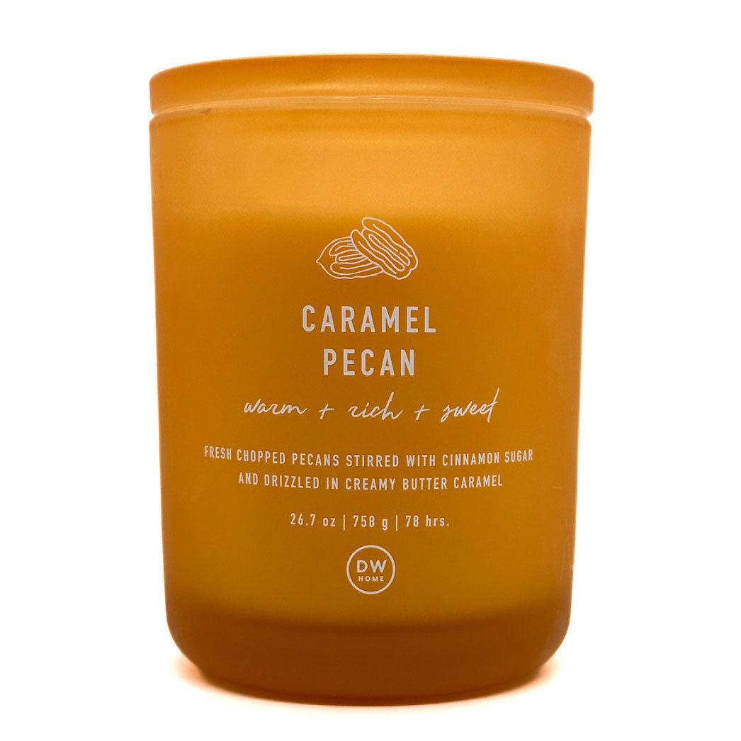 A DW Home Caramel Pecan scented candle in a matte amber-coloured jar with white text and a line drawing of pecans on the front, set against a plain white background.