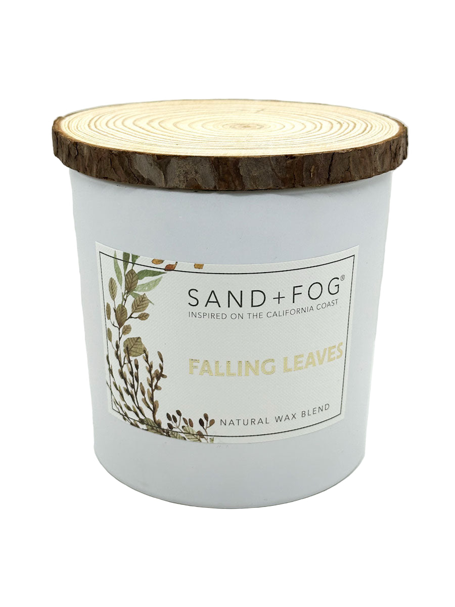Candle with a wooden lid labeled 'Sand + Fog Falling Leaves' on a white background