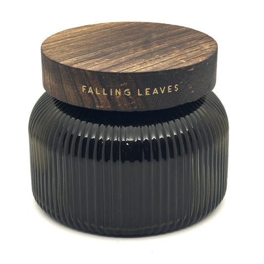 A dark ribbed glass jar candle with a round wooden lid printed with the scent name 'FALLING LEAVES' in gold lettering, set against a plain white background.