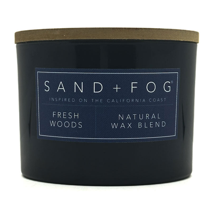 Fresh Woods blue candle with a label reading 'Sand + Fog' on a white background