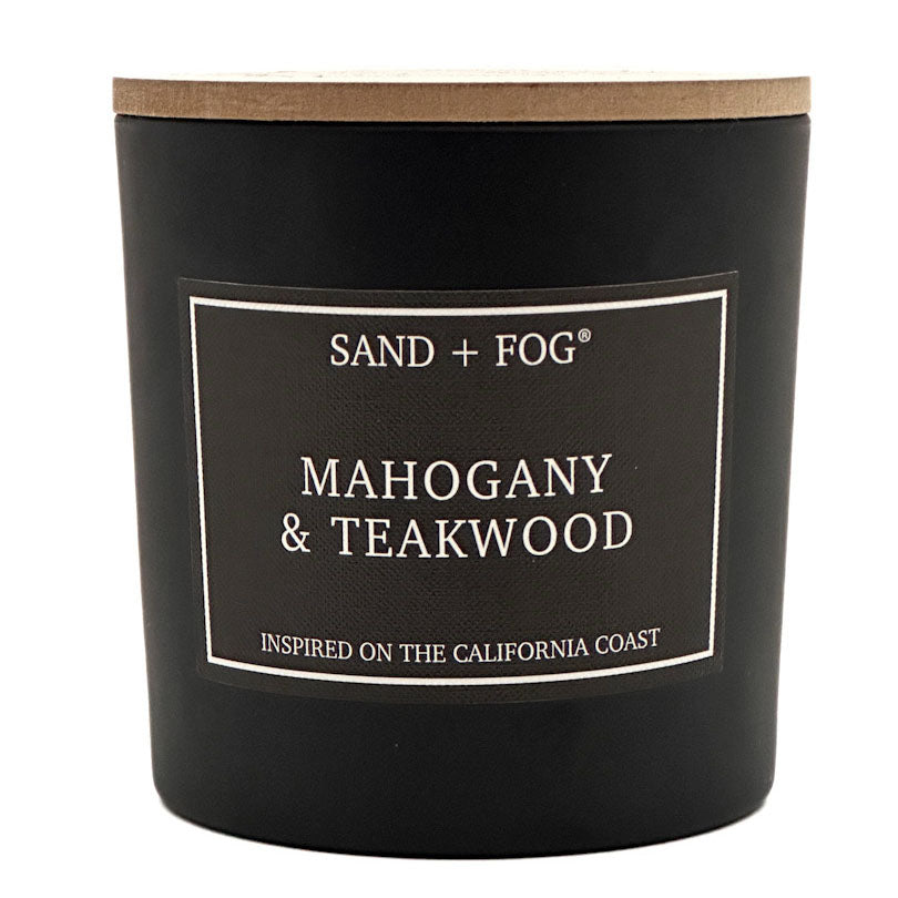 A black jar candle with a light wood lid and a black label reading 'SAND + FOG' and 'MAHOGANY & TEAKWOOD' on a white background.