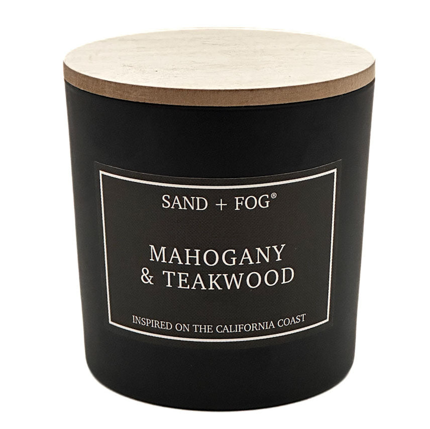 A black jar candle with a light wood lid and a black label reading 'SAND + FOG' and 'MAHOGANY & TEAKWOOD' on a white background.