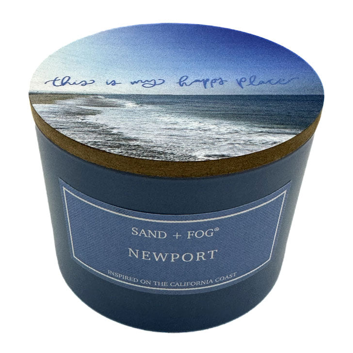 Candle container with beach scene lid and 'Sand + Fog Newport' label on a white background
