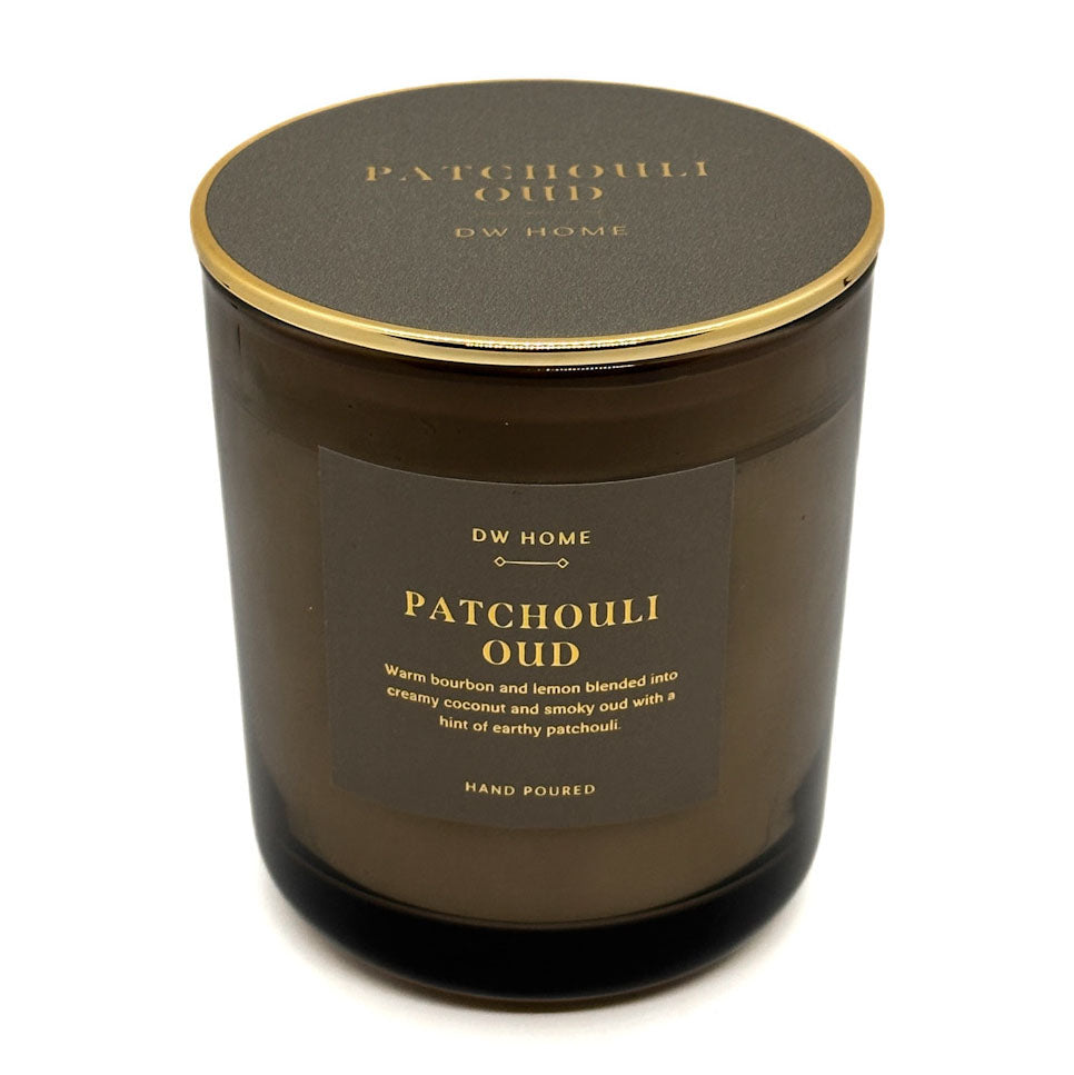 DW Home Patchouli Oud candle in an amber glass jar with a gold-rimmed lid and a dark brown label, shown on a white background.