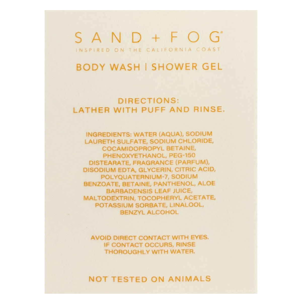 A beige rectangular card with orange text reading 'SAND + FOG' and 'BODY WASH | SHOWER GEL,' plus directions and ingredients, photographed against a white background.