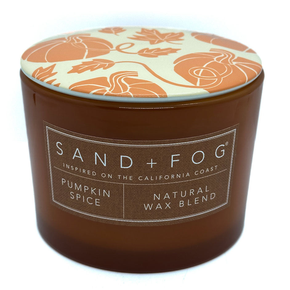 Candle jar with decorative lid featuring pumpkin patterns, labeled 'Sand + Fog' on a white background.