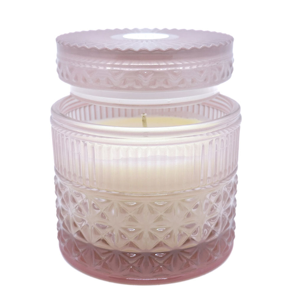 Decorative candle in a textured glass jar with a white lid on a white background