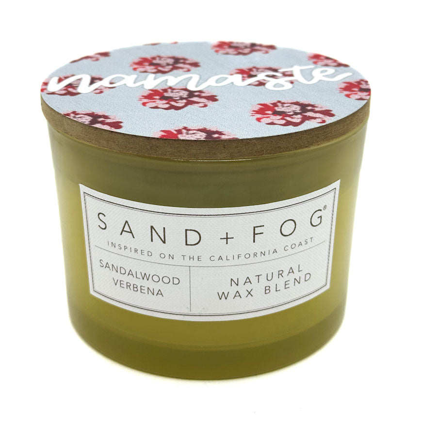 Sandalwood Verbena Olive Green candle with floral lid labeled 'Namaste' by Sand + Fog' on a white background