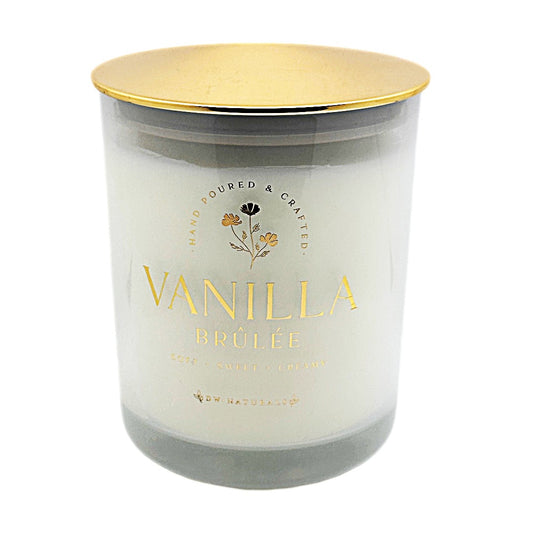 A glass jar candle with a metallic gold lid and a frosted white wax body, featuring gold foil text that reads 'VANILLA BRÚLÉE' and 'HAND POURED & CRAFTED' on a clean white background.