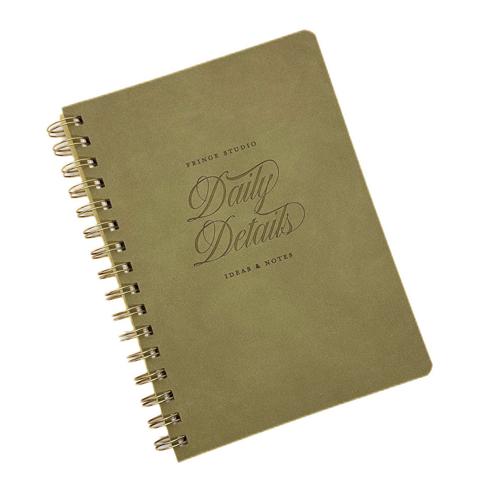 An olive green A5 spiral-bound notebook with gold-toned wire binding and embossed text reading 'PRINCE STUDIO Daily Details IDEAS & NOTES' on a white background.