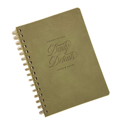 An olive green A5 spiral-bound notebook with gold-toned wire binding and embossed text reading 'PRINCE STUDIO Daily Details IDEAS & NOTES' on a white background.