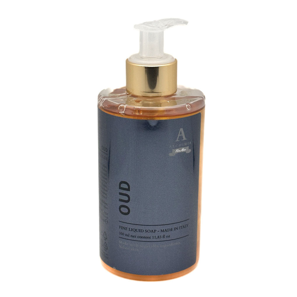 A bottle of Alchimia Oud Fine Liquid Soap, featuring a dark slate blue label, a metallic gold pump collar, and a clear pump dispenser, filled with amber-coloured liquid, set against a plain white background.