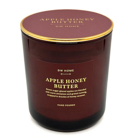 A DW Home Apple Honey Butter scented candle in a dark amber glass jar with a gold rim and a matching dark maroon lid, shown on a white background.