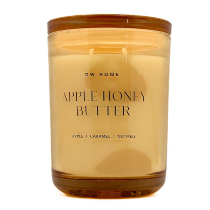 A candle in a translucent amber glass jar with a matching amber lid, labeled 'DW HOME APPLE HONEY BUTTER' on a clean white background.