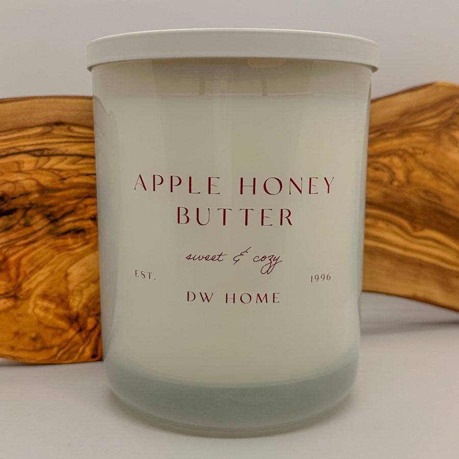 Candle labeled 'Apple Honey Butter' by DW Home on a wooden surface.