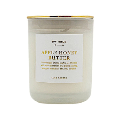 A glass jar candle with a white wax body, a white label reading 'DW HOME APPLE HONEY BUTTER,' and a gold metal lid, shown on a plain white background.