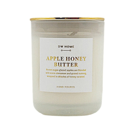 A glass jar candle with a white wax body, a white label reading 'DW HOME APPLE HONEY BUTTER,' and a gold metal lid, shown on a plain white background.
