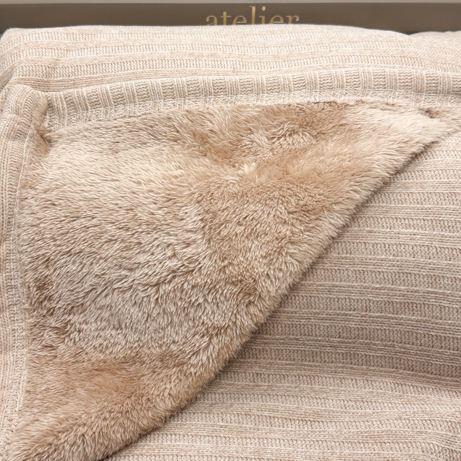 Close-up of a beige knit blanket with a soft plush sherpa lining, folded over to show the texture.