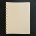 Fringe Studio beige notebook with gold spiral binding on a black background
