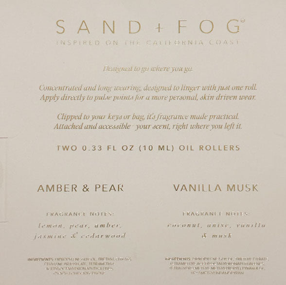 A beige product card or packaging insert for Sand + Fog oil rollers, featuring scent names Amber & Pear and Vanilla Musk with descriptive text and scent notes in a gold-toned serif font.