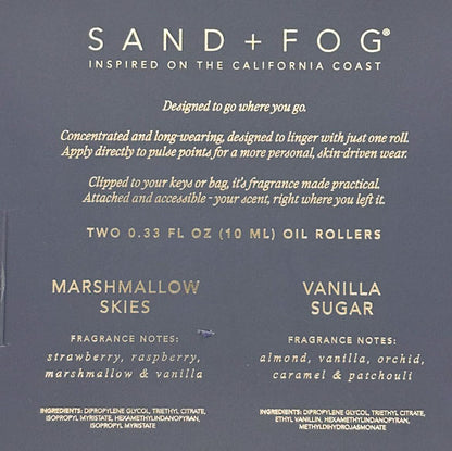 Back of a Sand + Fog oil roller package in a dark slate blue-gray color, showing product details, scent notes for Marshmallow Skies and Vanilla Sugar, and usage text in white and gold lettering.