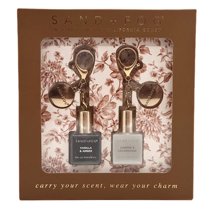 Sand + Fog carry your scent, wear your charm set in a brown floral gift box. The set includes a Vanilla & Amber vanilla perfume oil and a Jasmine & Cedarwood eau de parfum oil, each with a gold-toned keychain charm.