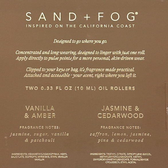 The back of a Sand + Fog oil roller packaging card, featuring a warm brown background with white text detailing the scent profiles of Vanilla & Amber and Jasmine & Cedarwood.