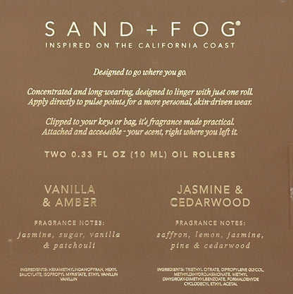 The back of a Sand + Fog oil roller packaging card, featuring a warm brown background with white text detailing the scent profiles of Vanilla & Amber and Jasmine & Cedarwood.