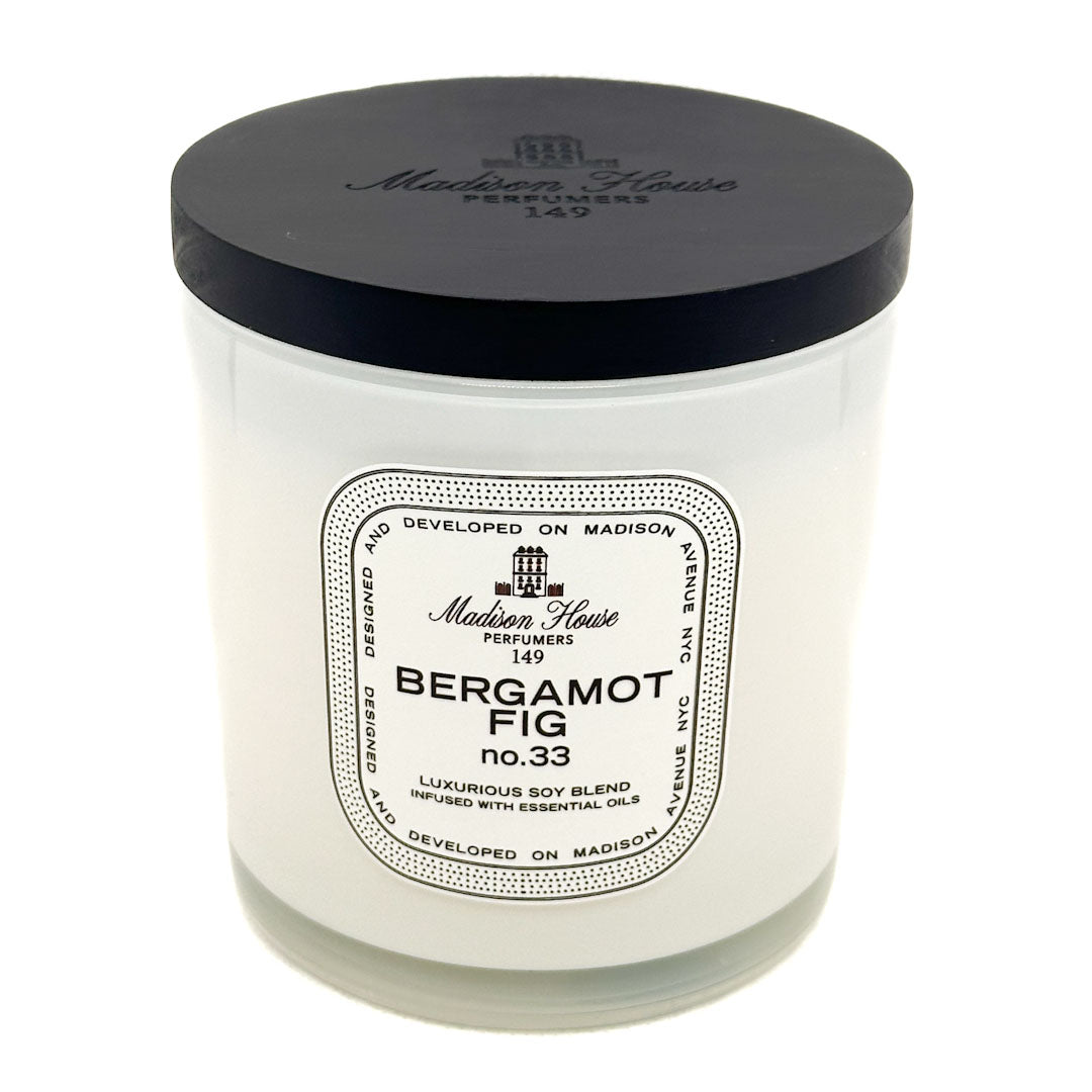 A white glass jar candle with a black lid, featuring a white paper label that reads 'Bergamot Fig no.33' by Madison House Perfumers 149.