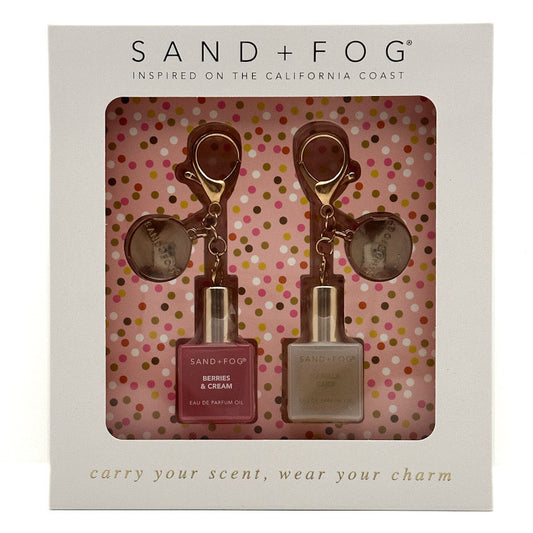 Sand + Fog  gift set in its original white packaging, featuring a mini berry and cream and vanilla cake perfume oil bottles and a matching keychain with a rose gold keyring and circular charm.