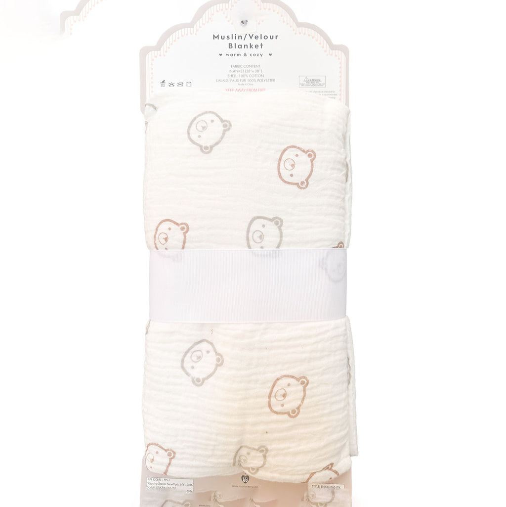 A folded muslin/velvet baby blanket with a cute teddy bear face pattern, packaged in its original retail card packaging with a white paper band around the middle.