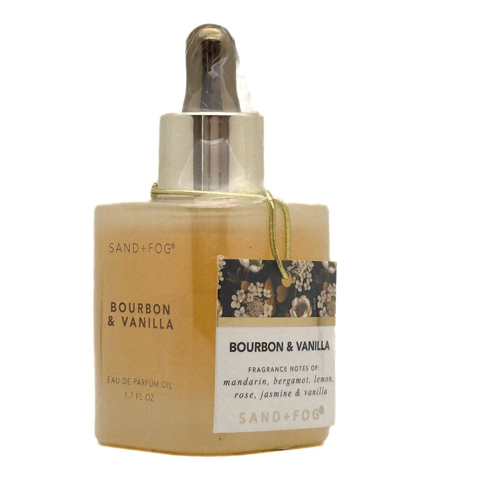 A bottle of Sand + Fog Bourbon & Vanilla Eau de Parfum Oil, featuring a square amber-colored glass bottle with a gold-tone dropper cap and a hanging paper label.
