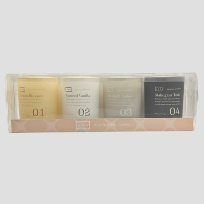 Four LAB scented candles in a clear plastic window box with a pink patterned base. The candles are labeled Lemon Blossom, Sugared Vanilla, Midnight Amber, and Mahogany Teak, numbered 01 to 04.
