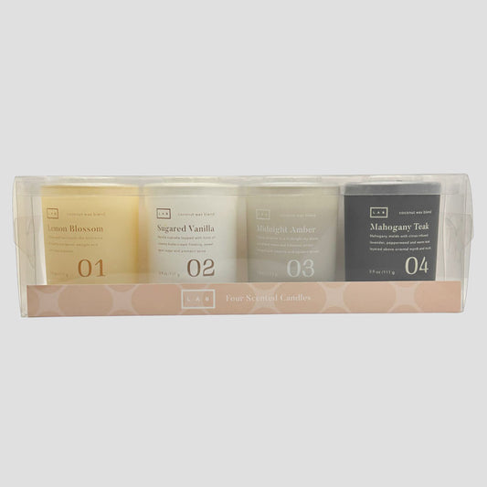 Four LAB scented candles in a clear plastic window box with a pink patterned base. The candles are labeled Lemon Blossom, Sugared Vanilla, Midnight Amber, and Mahogany Teak, numbered 01 to 04.