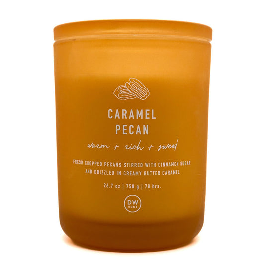 A DW Home Caramel Pecan scented candle in a matte amber-coloured jar with white text and a line drawing of pecans on the front, set against a plain white background.