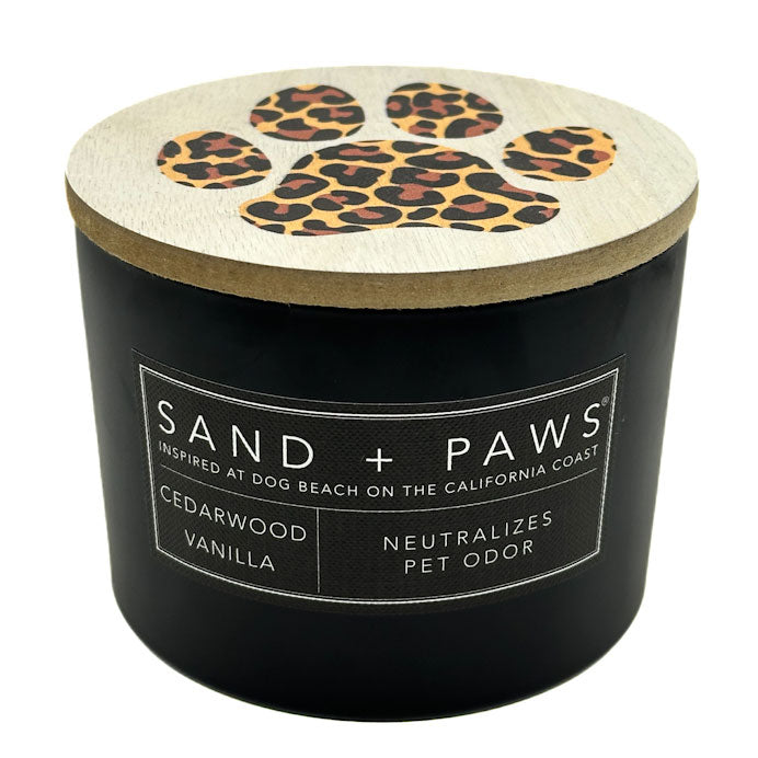 Black Cedarwood Vanilla Scented Candle with leopard print paw design on lid, labeled 'Sand + Paws'.