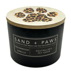 Black Cedarwood Vanilla Scented Candle with leopard print paw design on lid, labeled 'Sand + Paws'.