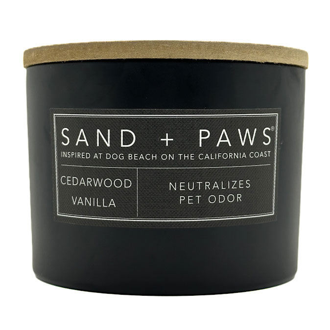Black cedarwood vanilla candle with a wooden lid labeled 'Sand + Paws' on a white background