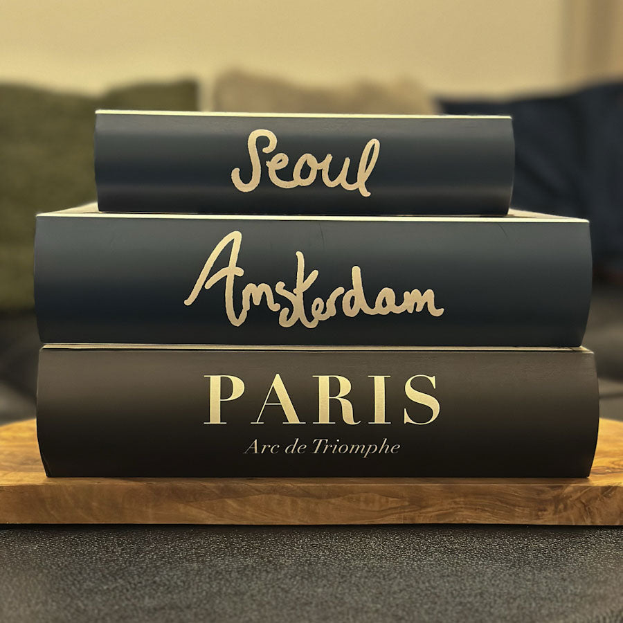 Stack of keepsake book boxes with 'Seoul', 'Amsterdam', and 'Paris' on a wooden surface