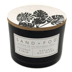 Coconut & Palm black candle with a decorative lid featuring leaf patterns and a visible label on a white background.
