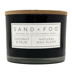Coconut & Palm black candle with a label reading 'Sand + Fog' on a white background