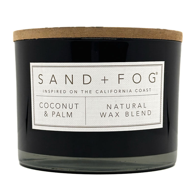 Coconut & Palm black candle with a label reading 'Sand + Fog' on a white background