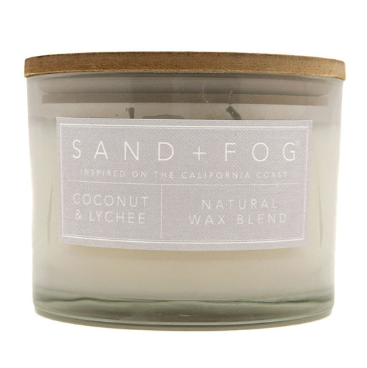 SAND + FOG Coconut & Lychee candle with a wooden lid and label on a white background