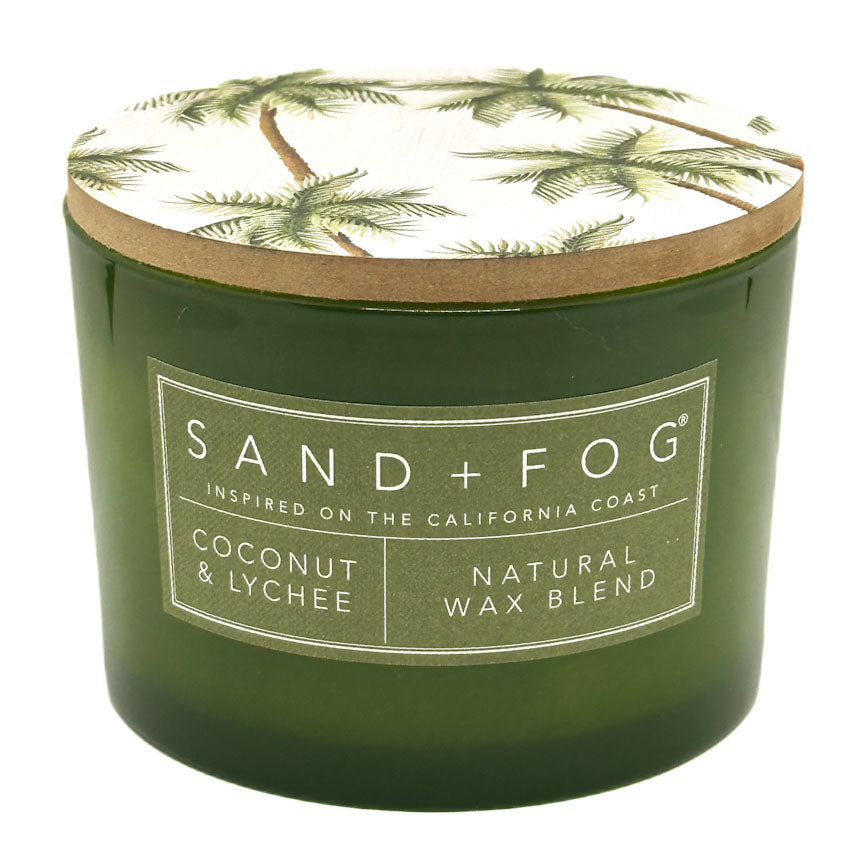 Coconut & Lychee green candle with a decorative lid featuring palm trees, branded 'Sand + Fog'.