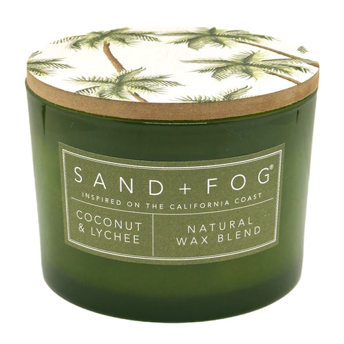 Coconut & Lychee green candle with a decorative lid featuring palm trees, branded 'Sand + Fog'.