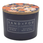 Coconut & Palm candle with floral lid and 'Sand + Fog' label on a white background