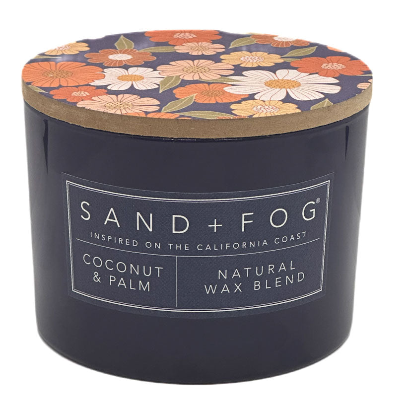 Coconut & Palm candle with floral lid and 'Sand + Fog' label on a white background