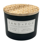 Coconut & Palm black candle with a patterned wooden lid labeled 'Sand + Fog' on a white background